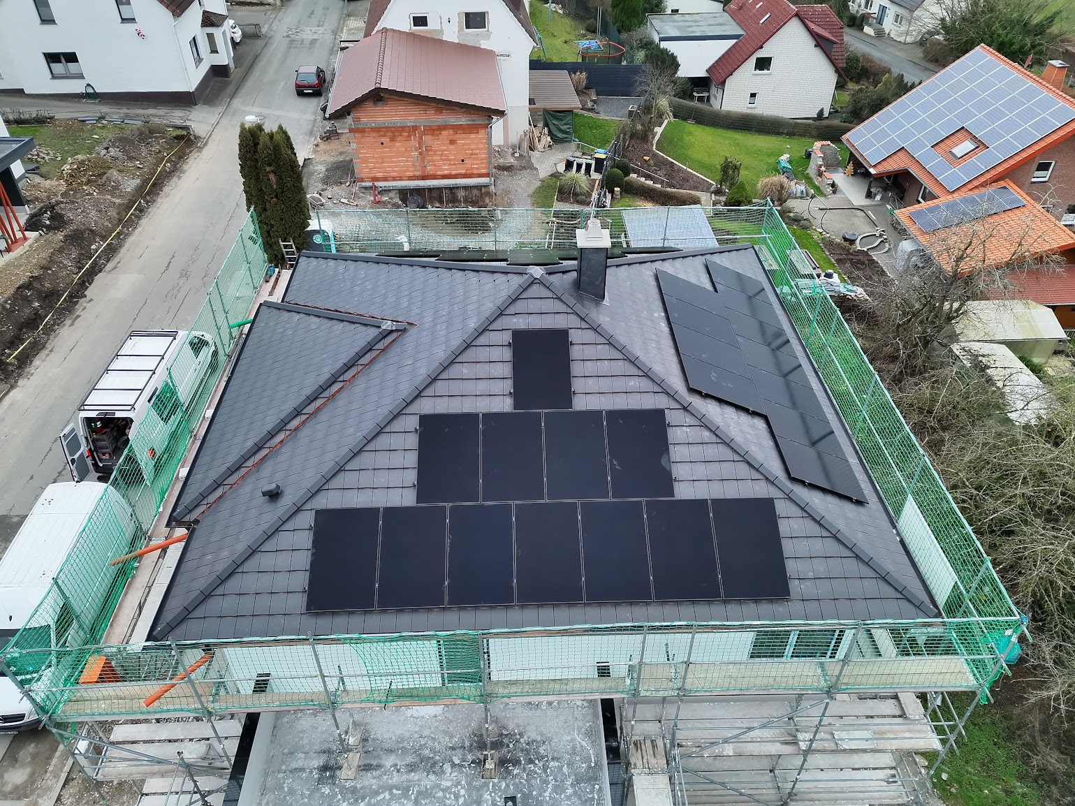 Luftaufnahme einer Photovoltaikanlage auf dem Walmdach eines eingerüsteten Neubaus