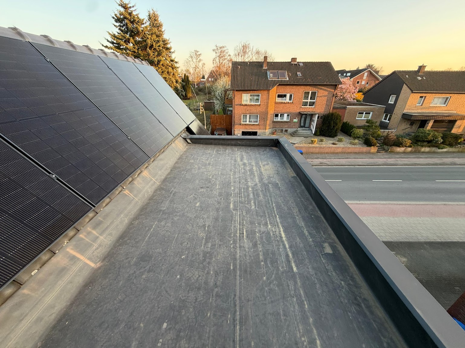 Photovoltaikmodule auf einer steilen Dachfläche neben einem Flachdach-Anbau im Abendlicht