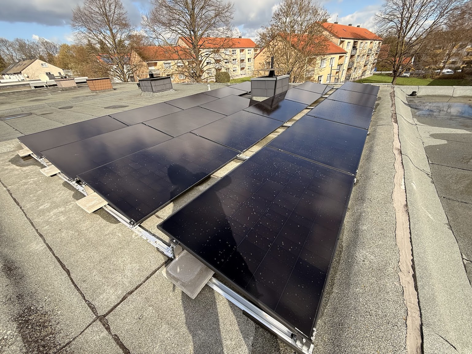 Neu montierte Photovoltaikmodule auf einem Flachdach mit Blick auf umliegende Wohngebäude